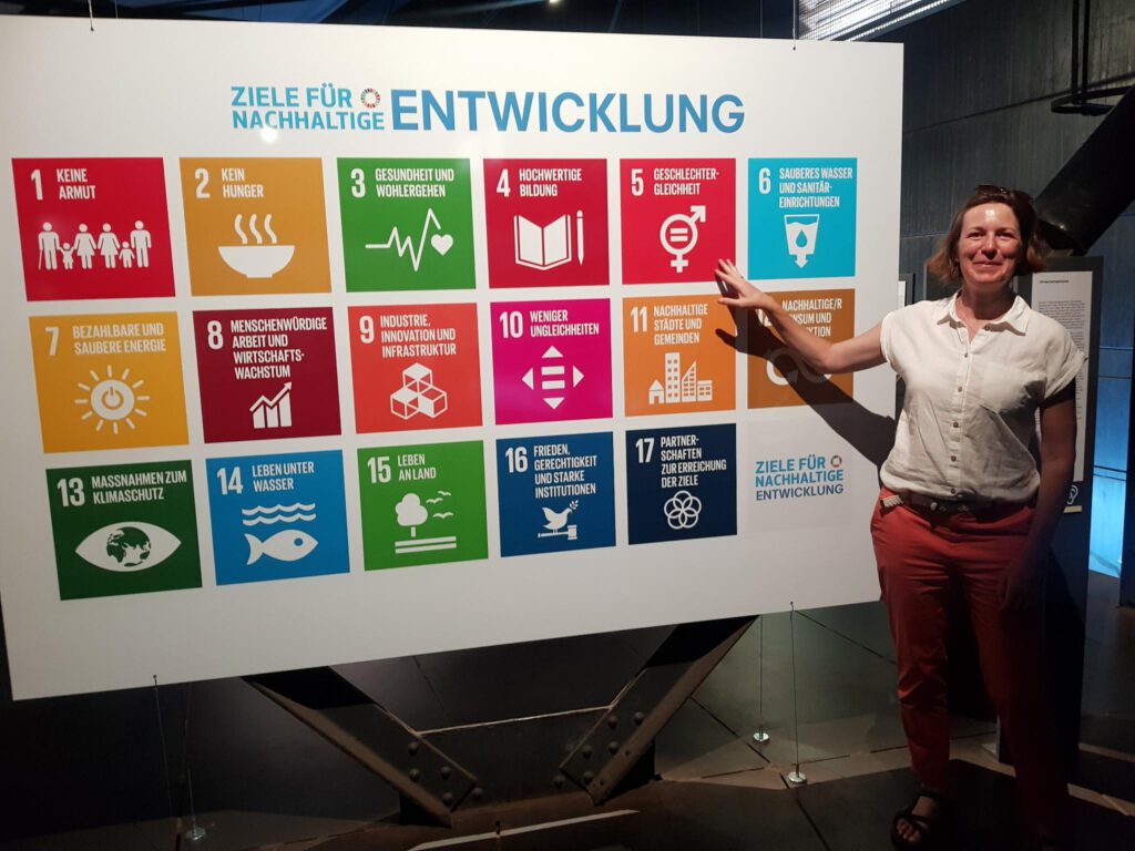 Inga vor einem Bild mit den 17 Nachhaltigkeitszielen der Vereinten Nationen